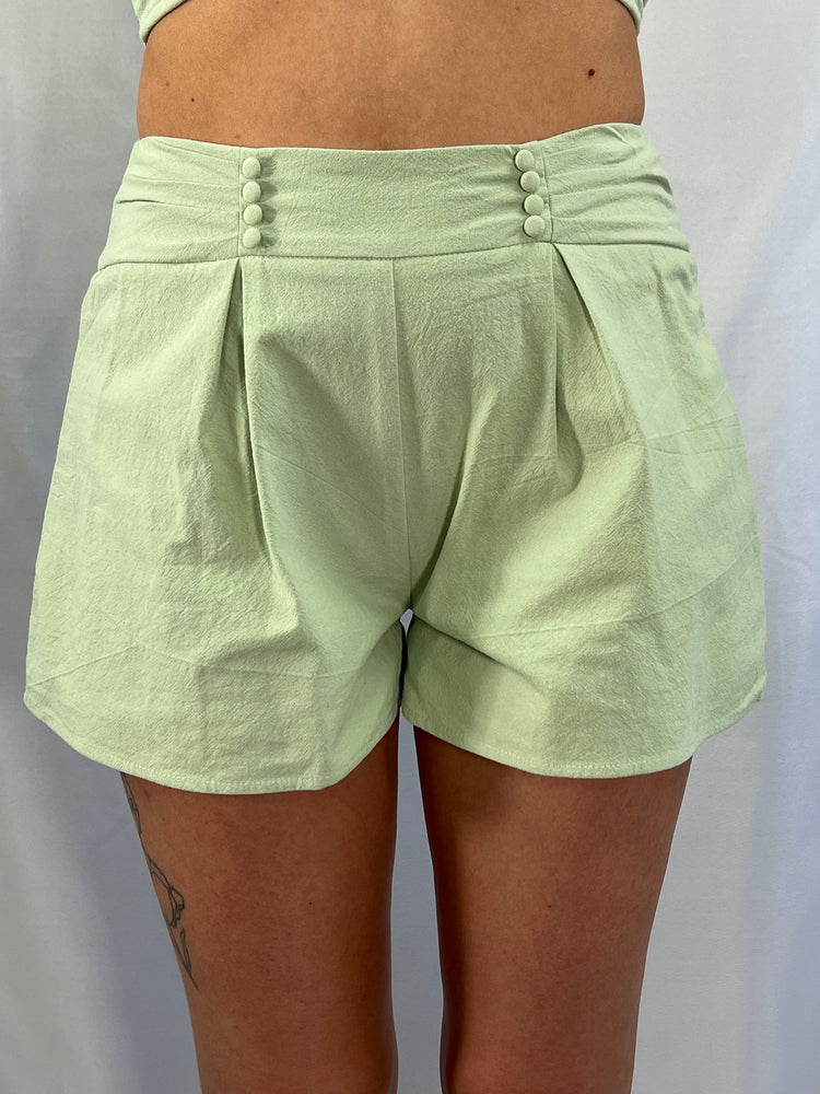 sage green shorts featuring 100% cotton woven fabric, pleated front, cover button details with pleated waist band. Back zipper and hook and eye access. Lining polyester.