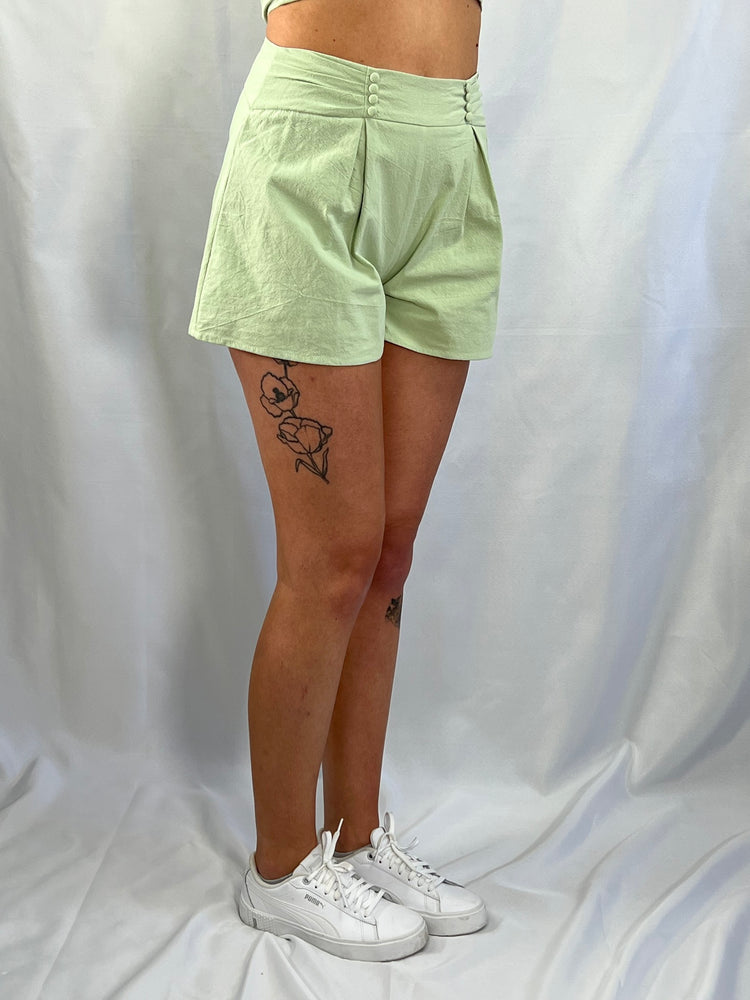 sage green shorts featuring 100% cotton woven fabric, pleated front, cover button details with pleated waist band. Back zipper and hook and eye access. Lining polyester.